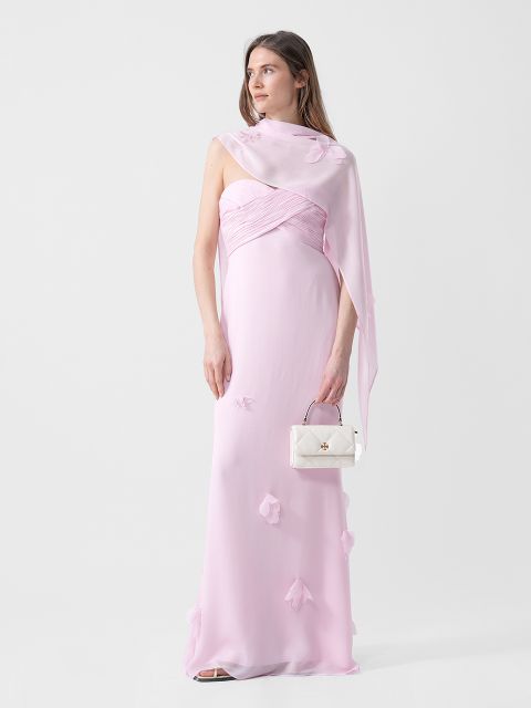 Eine Frau in einem hellrosa, trägerlosen Kleid mit Blumendetails hält eine kleine weiße Handtasche und trägt ein passendes durchsichtiges Tuch über einer Schulter.