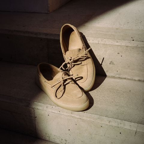 Ein Paar beigefarbene Bootsschuhe aus Wildleder mit Schnürsenkeln, die auf sonnenbeschienenen Betonstufen ruhen.