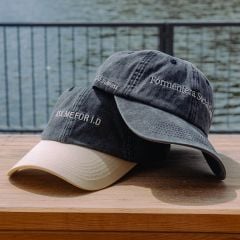 Zwei Baseballkappen auf einer Holzfläche am Wasser; auf der einen steht "ASK ME FOR ID" und auf der anderen "Formentera Social Club".