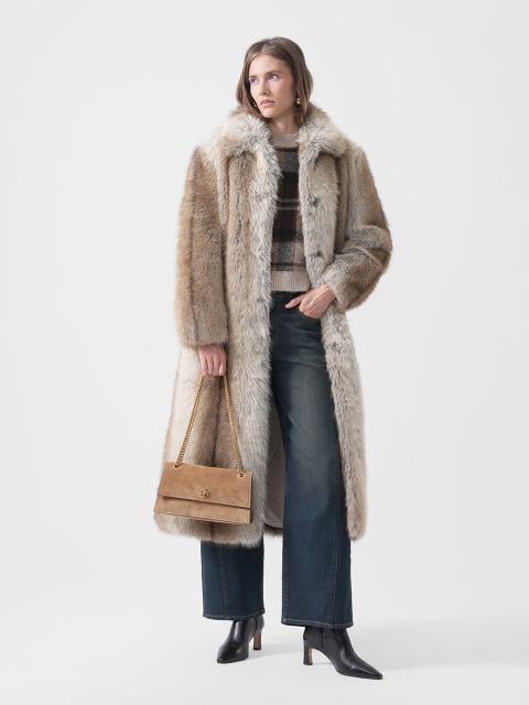 Ein Model trägt einen langen Kunstpelzmantel, einen karierten Pullover, eine Jeans mit weitem Bein und schwarze Stiefeletten sowie eine hellbraune Umhängetasche mit einem goldenen Kettenriemen.