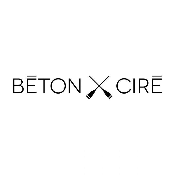 Logo mit dem Text „BÉTON CIRÉ“ in schwarzen Großbuchstaben auf weißem Hintergrund. Zwischen den Wörtern befindet sich ein schwarzes, durchgekreuztes, werkzeugähnliches Symbol.