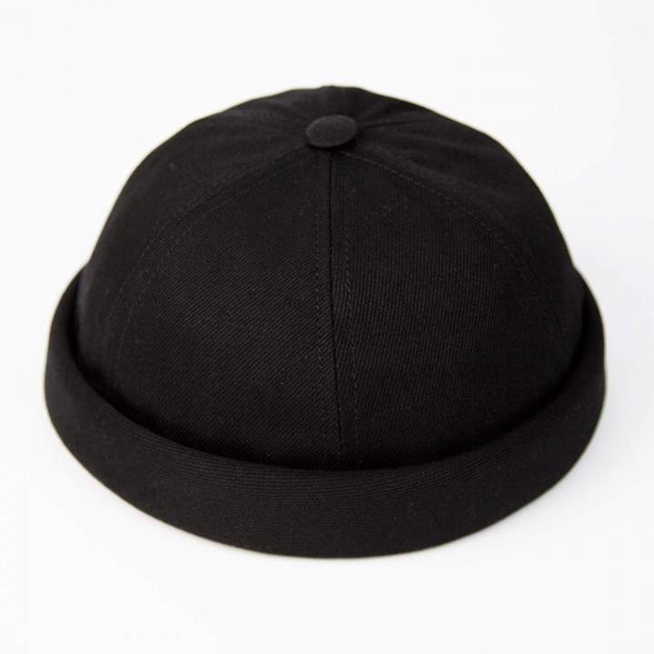 Eine schwarze, runde, randlose Mütze mit kurzem, hochgeschlagenem Rand, die oft als Beanie-Mütze bezeichnet wird. Sie hat ein einfaches, minimalistisches Design auf weißem Hintergrund.