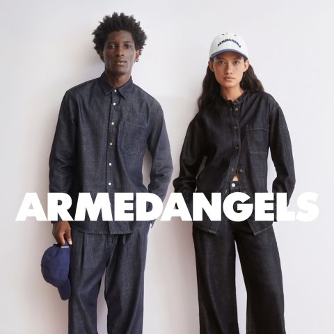 Zwei Models in dunklen Jeanshemden und -hosen stehen vor einem weißen Hintergrund mit der Aufschrift "ARMEDANGELS". Ein Modell hält eine blaue Kappe.