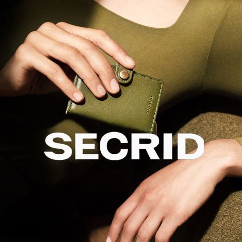 Eine Person in Grün hält eine kleine olivgrüne SECRID-Brieftasche in der Hand, auf der in fetten weißen Buchstaben "SECRID" steht.