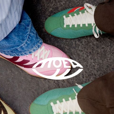 Nahaufnahme von zwei Paar bunten Turnschuhen auf einem strukturierten Boden mit fettem weißem Text "MoEa" in der Mitte überlagert.