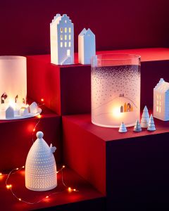 Keramikhäuser, Bäume und Teelichthalter sind auf roten Stufen angeordnet und werden von Lichterketten und Kerzenlicht sanft beleuchtet. Die Szene erinnert an eine gemütliche, festliche Winterdorfatmosphäre.