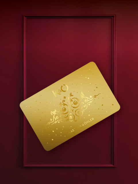 Eine goldene Karte mit einem verschnörkelten Muster und den Buchstaben "K&O" ist schräg auf einem weinroten Hintergrund mit rechteckigem Rahmen angebracht.
