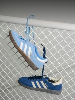 Zwei blaue Adidas-Turnschuhe mit weißen Streifen hängen an ihren Schnürsenkeln an einem weißen Metallzaun, einer hellblau und einer dunkelblau.