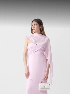 Frau in einem blassrosa, schulterfreien Abendkleid mit weißer Handtasche vor einem weißen Hintergrund mit grauem Farbverlauf oben.