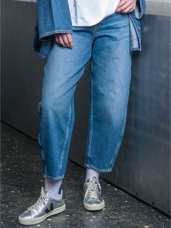 Eine Person, die blaue Jeans, eine Jeansjacke, weiße Socken und graue Turnschuhe trägt, steht in einem Haus neben einer Metallfläche.
