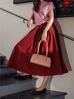 Eine Frau in einem gestreiften rosa Oberteil und einem roten Rock geht die Treppe hinunter, in der Hand eine blassrosa Handtasche und schwarze Schuhe.