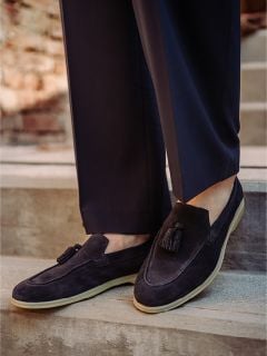 Eine Person, die dunkle Wildlederschuhe mit hellen Sohlen und eine dunkle Hose trägt, steht auf einer Außentreppe.