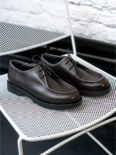 Ein Paar dunkelbraune Lederschnürschuhe steht auf einem weißen Metallgitterstuhl.