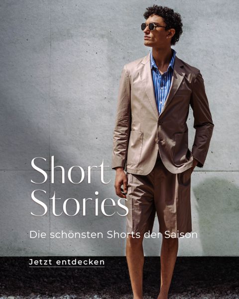 Ein Mann in einem braunen kurzen Anzug und einem gestreiften Hemd steht vor einer grauen Wand. Der Text lautet: "Kurzgeschichten. Die schönsten Shorts der Saison. Jetzt entdecken.